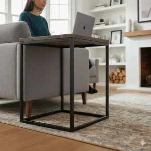 Close-up of a sturdy metal C-shaped side table base sliding underneath the fabric upholstery of a grey settee.