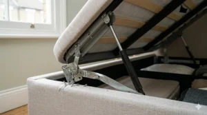 Detailed view of a king-size upholstered ottoman storage bed where the main metal hinge bar is bent and twisted, tearing away from the wooden frame.