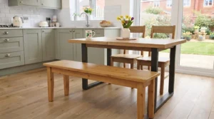 Traditional solid pine dining bench positioned alongside a matching wooden table in a bright country-style kitchen.