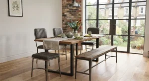 An industrial-style metal and timber dining bench and chair set combination set against a neutral feature wall.